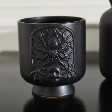 Black ceramic cup with spider web design on a reflective surface