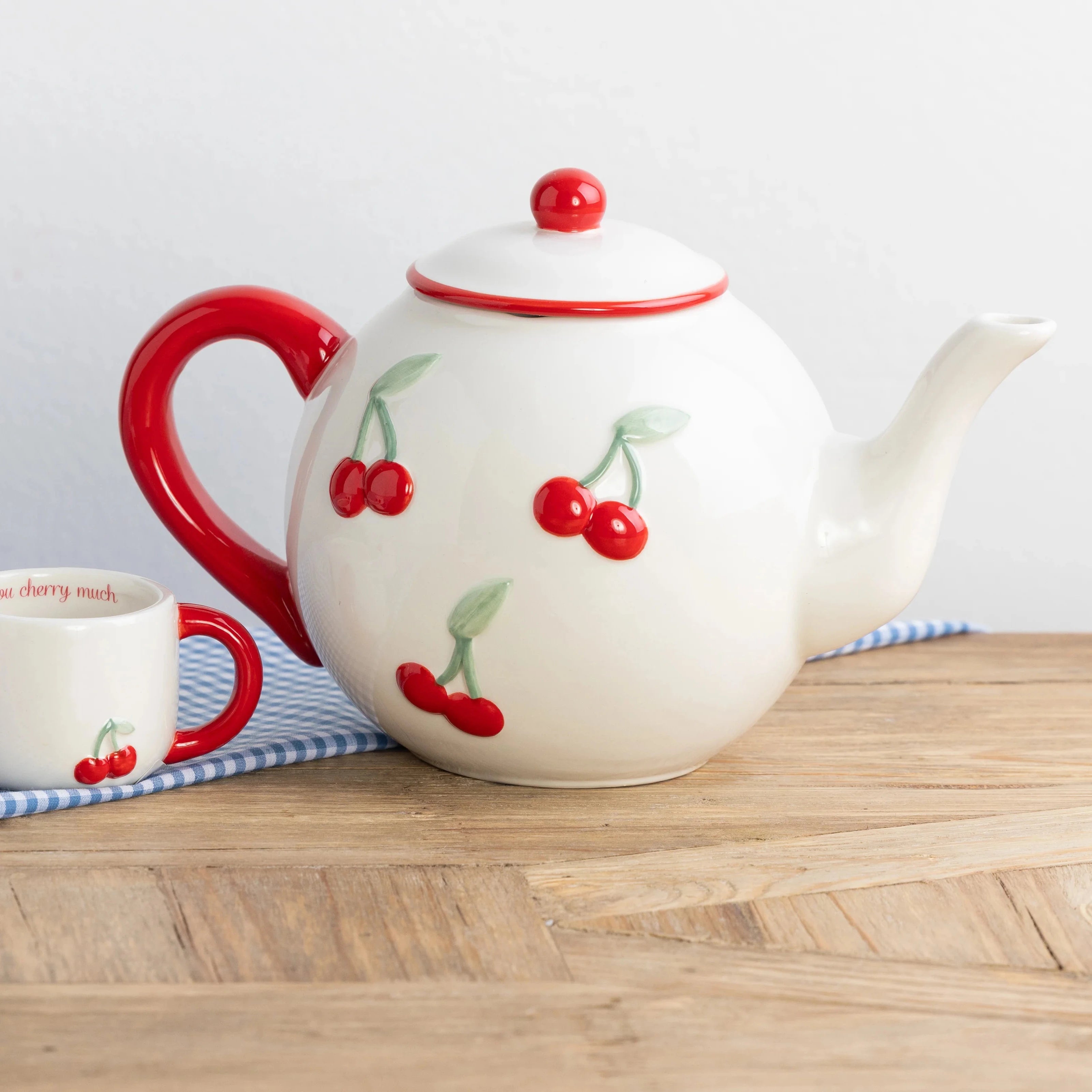 Teapot and mugs with cherry design on a wooden surface