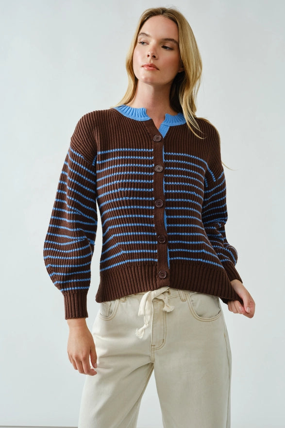 Woman wearing a brown and blue striped sweater with white pants on a light background
