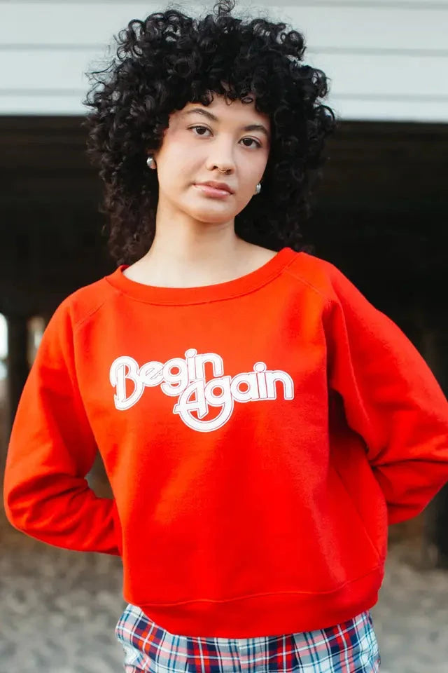 Person wearing a red sweatshirt with 'Begin Again' text, standing outdoors.