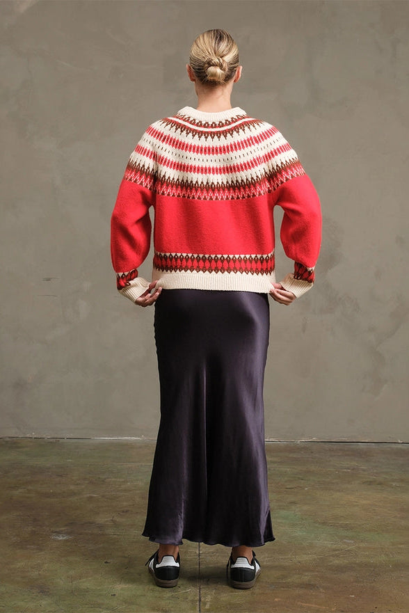Person wearing a red and white patterned sweater and dark purple skirt against a plain background