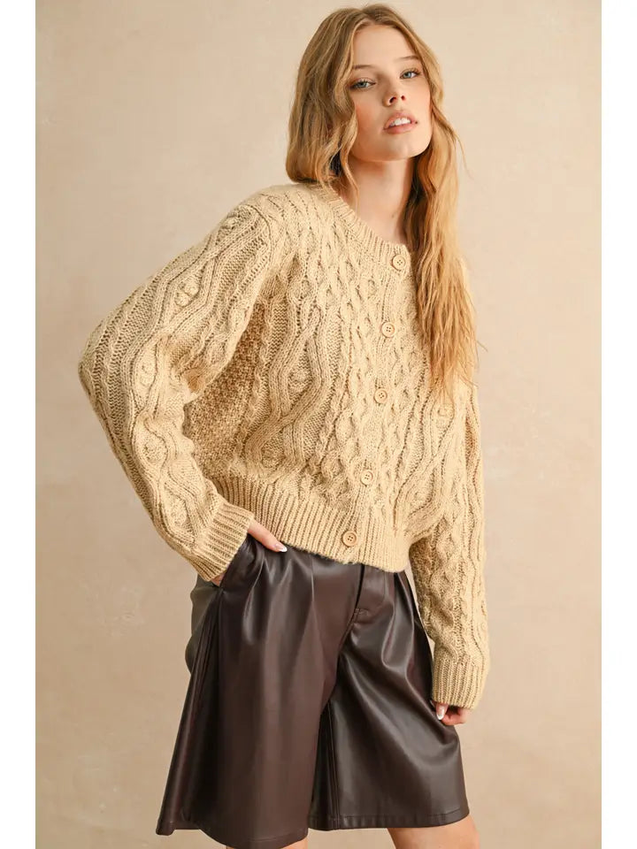 Woman wearing a beige cable knit sweater and brown leather skirt against a beige background