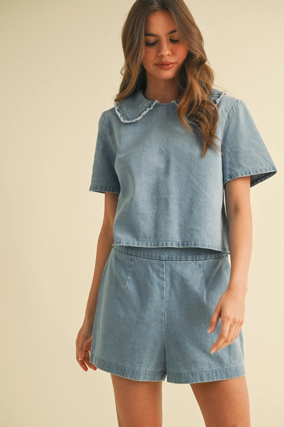 Woman wearing a light blue denim outfit with a collar on a beige background