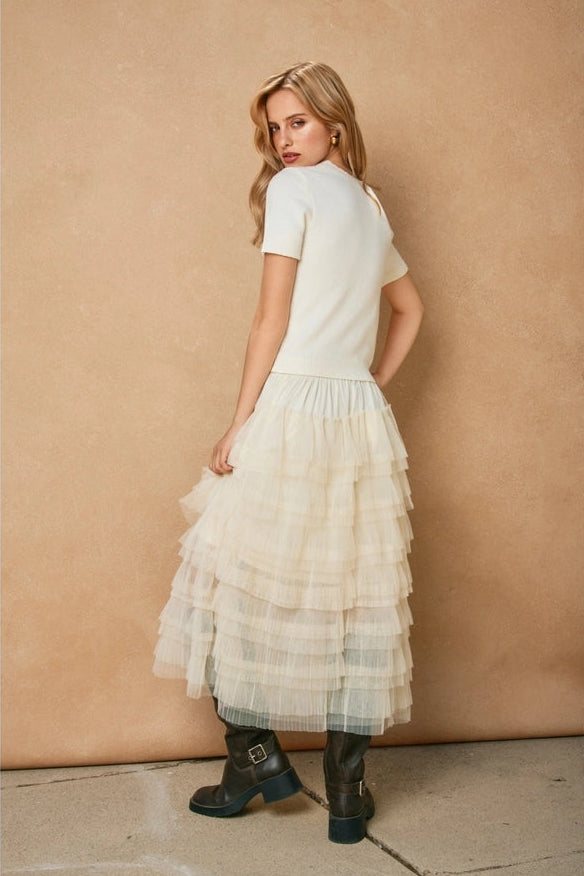 Woman wearing a white dress with a layered skirt against a beige wall.
