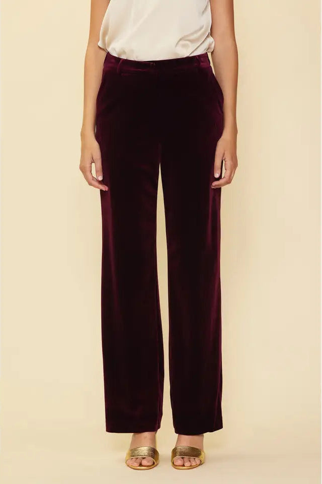 Person wearing burgundy velvet pants on a beige background