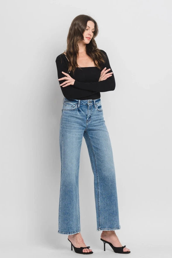 Woman wearing blue jeans and a black top against a plain background