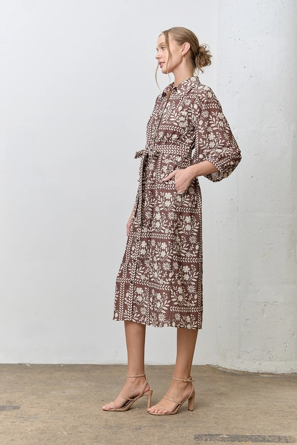 Woman wearing a patterned dress standing against a white wall.