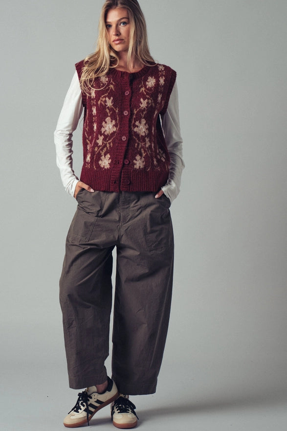 Woman wearing a floral embroidered vest over a white shirt with dark pants on a gray background