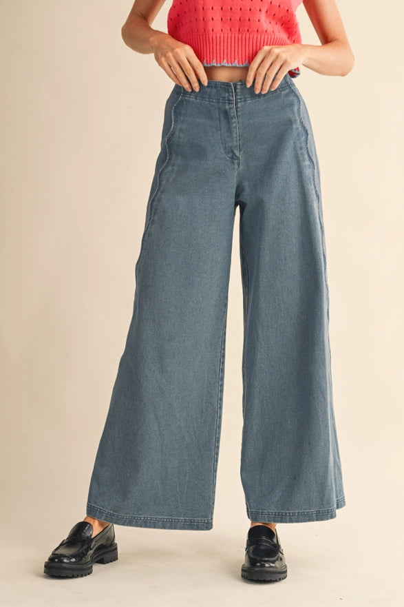 Person wearing blue wide-leg jeans and black shoes on a beige background