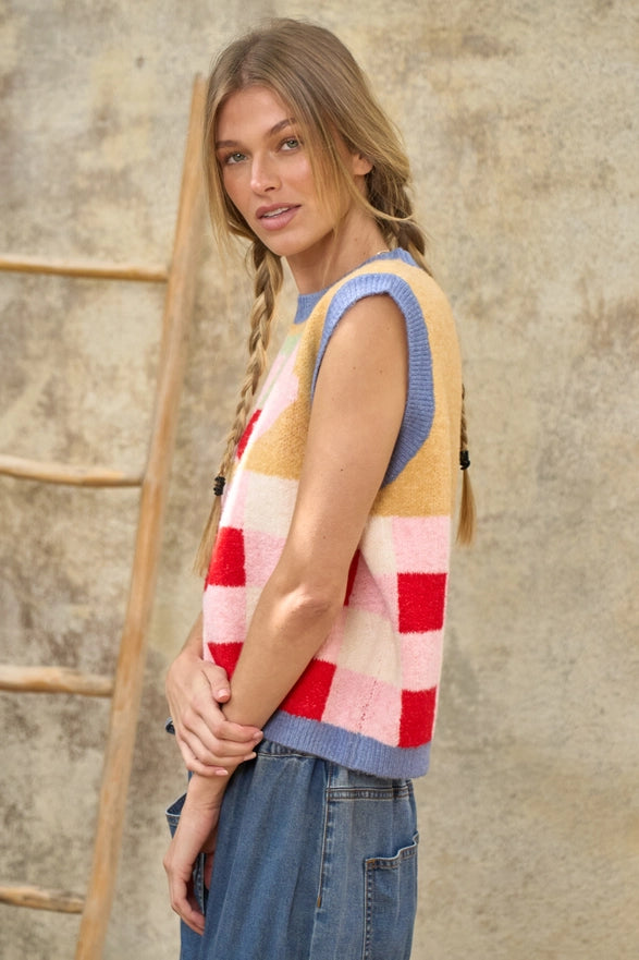 Woman wearing a colorful striped sweater vest against a textured wall.