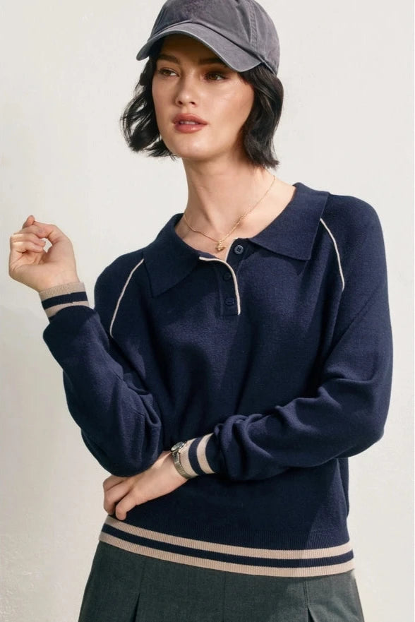 Woman wearing a navy blue sweater with white trim and a gray cap on a light background