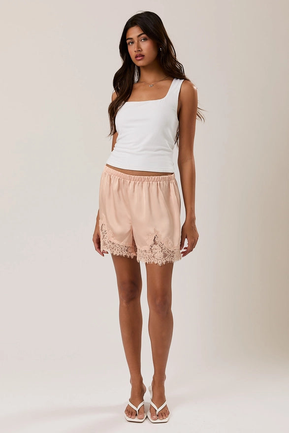 Woman wearing a white tank top and pink lace shorts on a plain background