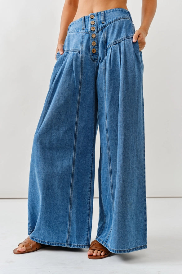 Wide-leg blue jeans with brown buttons on a white background