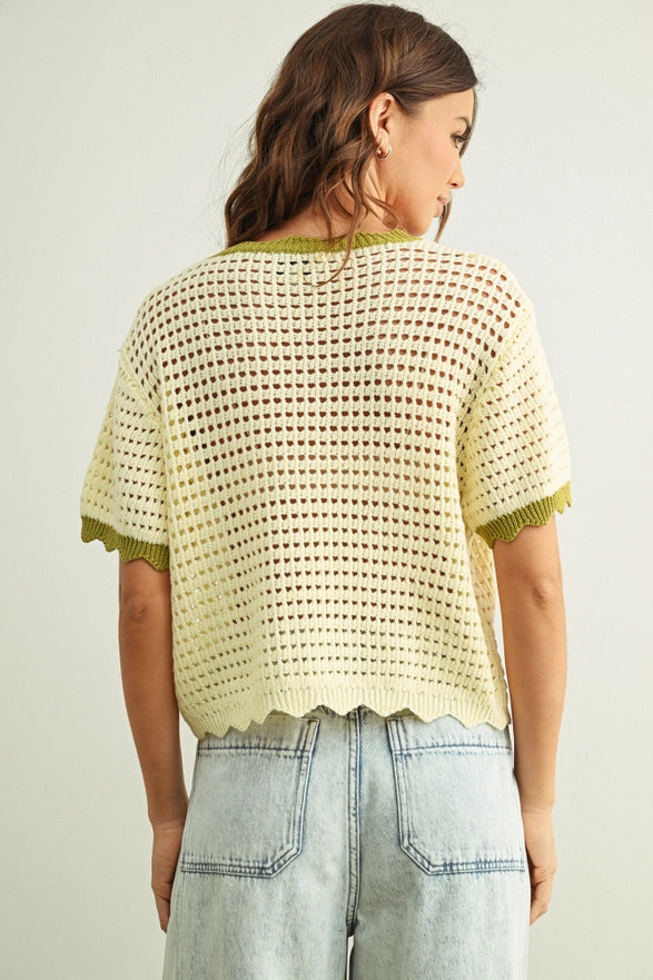 Woman wearing a light yellow crochet top with green trim on a plain background