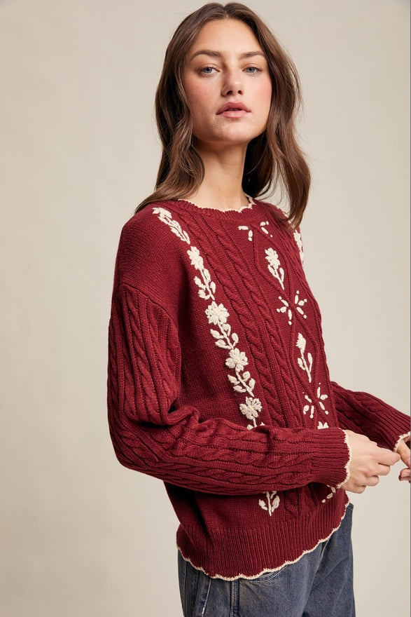 Woman wearing a burgundy sweater with floral patterns on a beige background