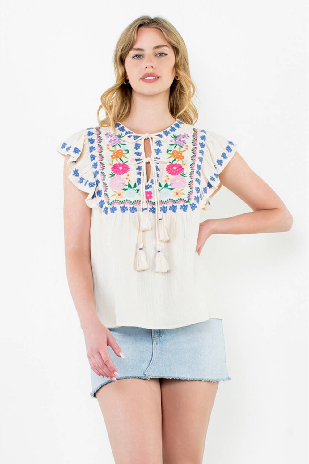 Woman wearing a white blouse with colorful floral embroidery on a white background