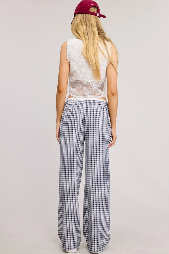 Person wearing a sleeveless top and checkered pants with a red cap on a plain background