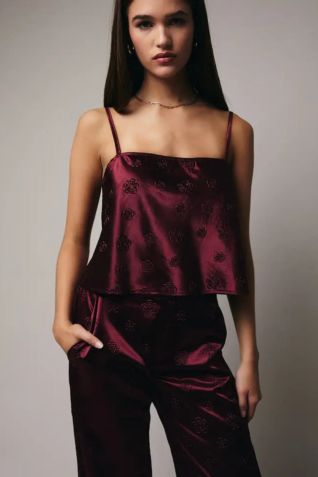 Woman wearing a burgundy satin pajama set against a gray background