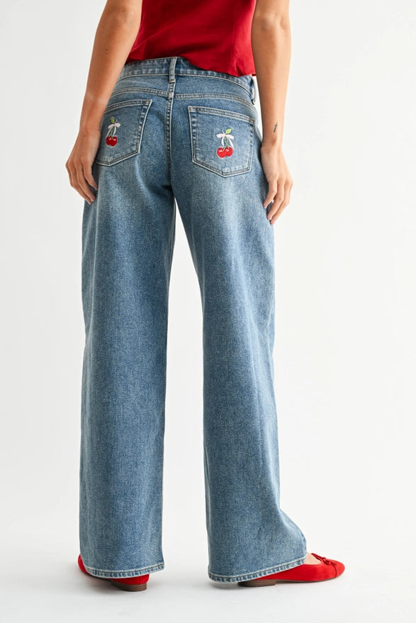 Person wearing blue jeans with cherry designs on a white background
