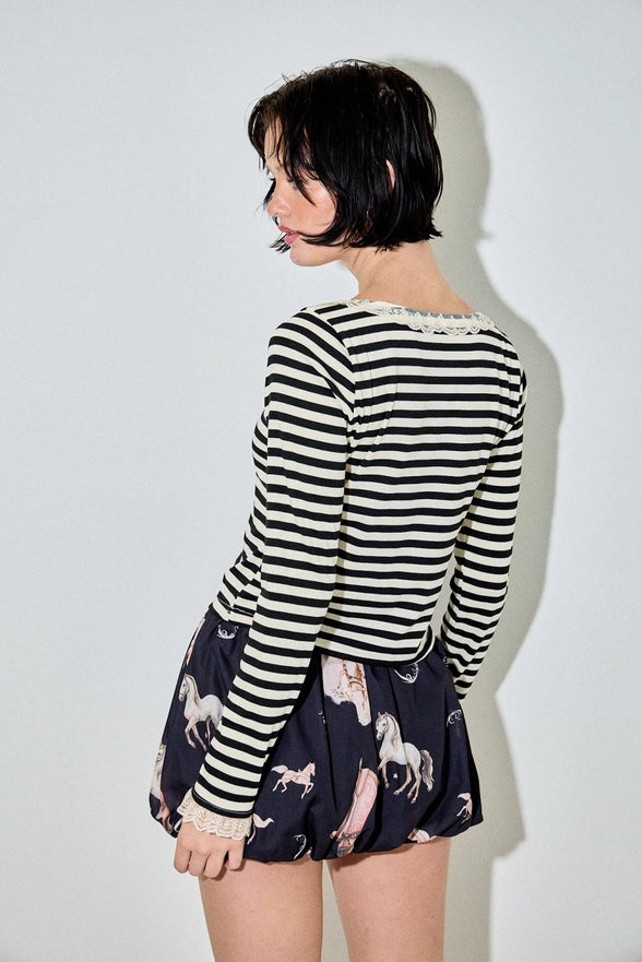 Person wearing a black and white striped shirt and a navy skirt with horse patterns on a plain background