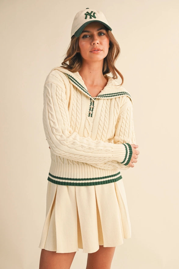 Woman wearing a cream-colored sweater with green accents and a matching skirt, paired with a cap.