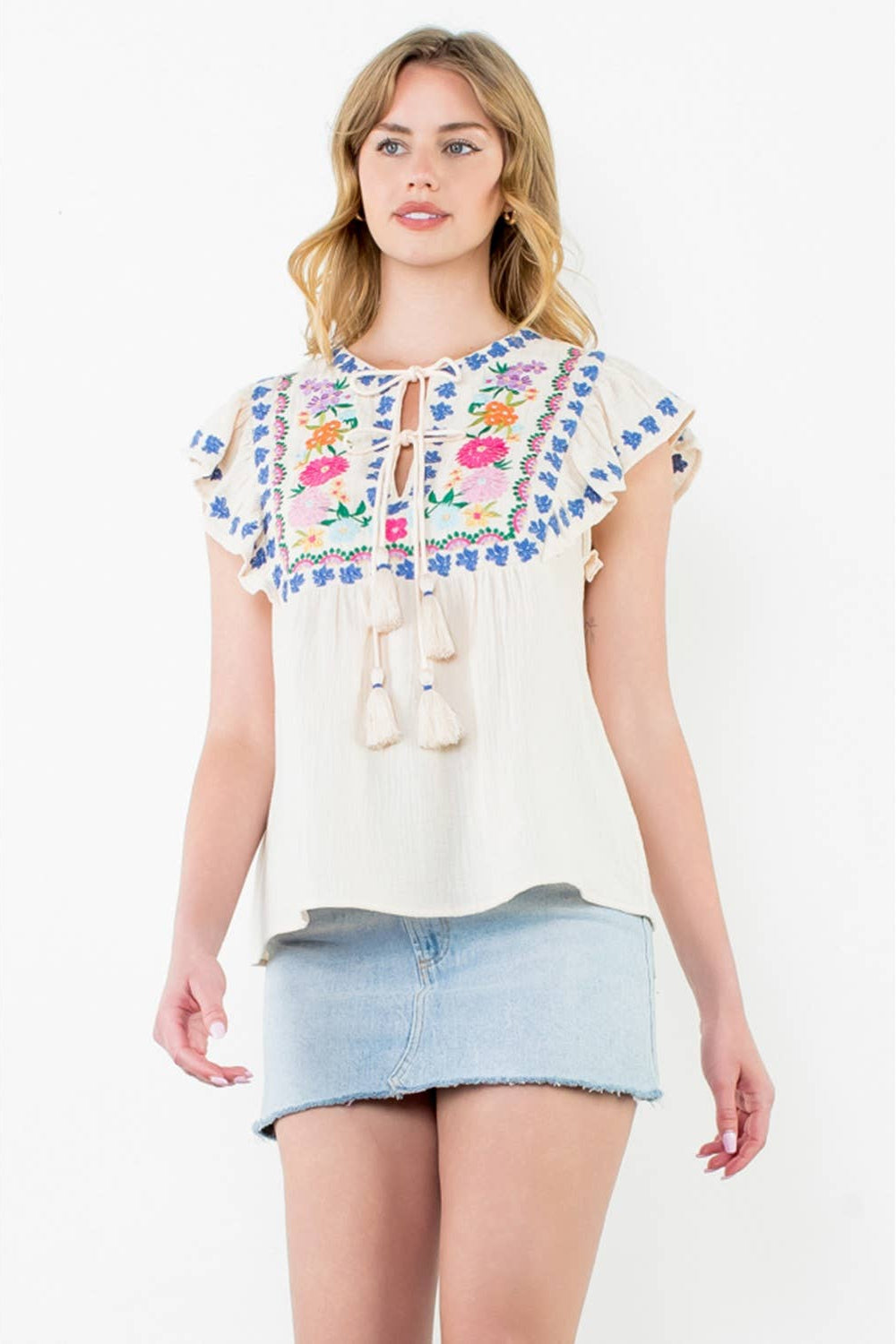 Woman wearing a white blouse with floral embroidery and a denim skirt on a white background
