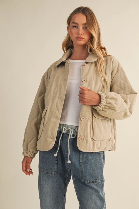 Woman wearing a beige jacket over a white shirt and blue jeans on a plain background