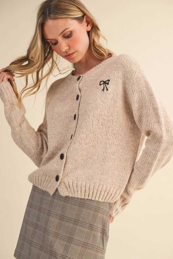 Woman wearing a beige cardigan with a black bow detail on a beige background