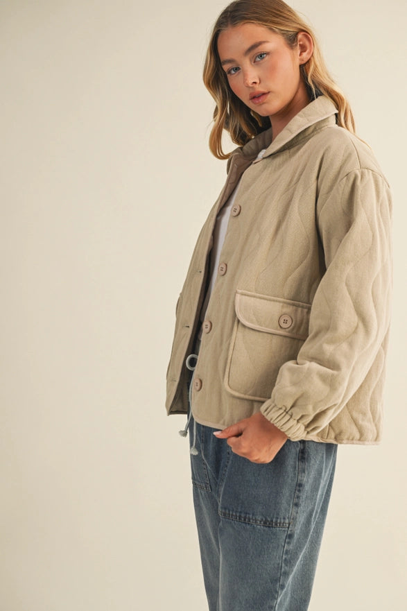 Woman wearing a beige jacket and blue jeans against a plain background