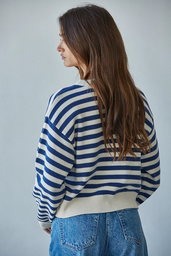 Woman wearing a blue and white striped sweater and blue jeans against a plain background