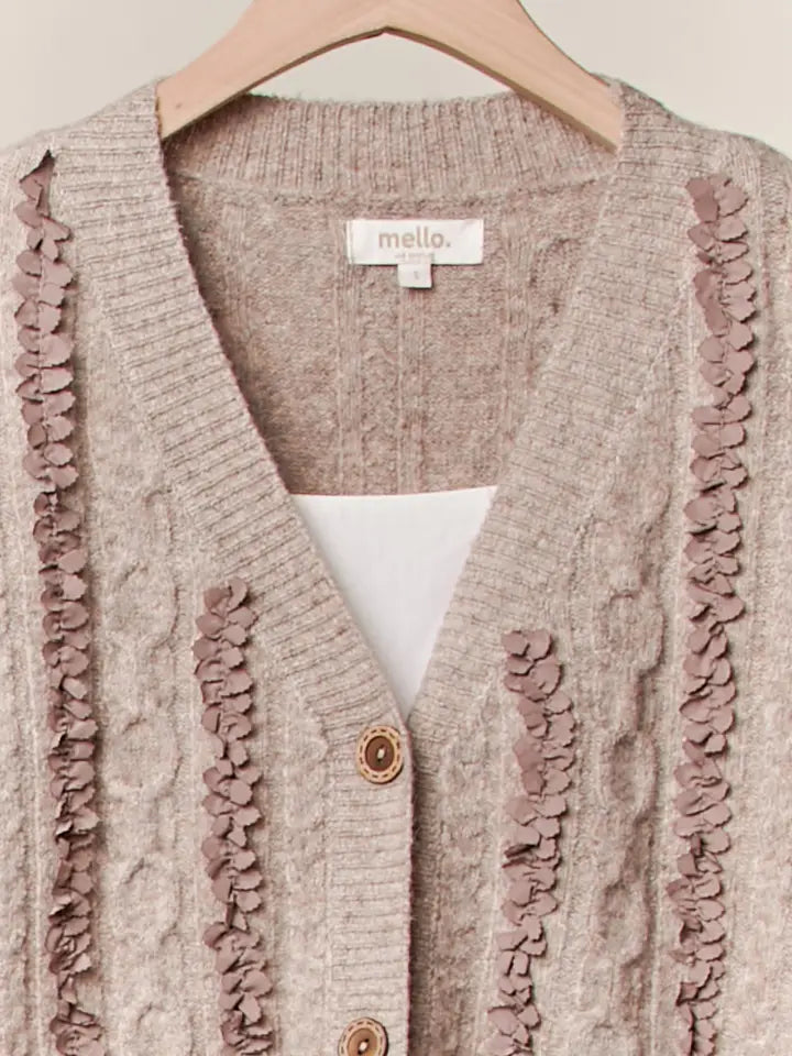 Cardigan with ruffled trim on a hanger, featuring the brand 'mello'.