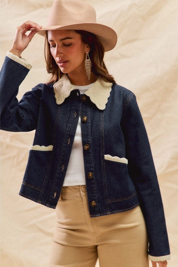 Woman wearing a denim jacket with white collar, beige hat, and earrings on a beige background