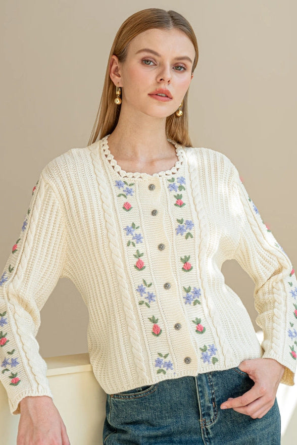 Woman wearing a cream-colored embroidered blouse with floral patterns against a neutral background