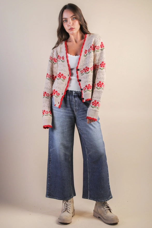 Woman wearing a floral cardigan, white top, blue jeans, and beige boots on a plain background