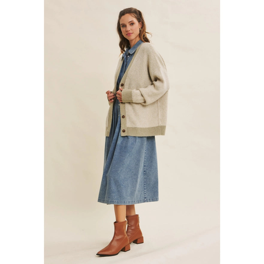 Woman wearing a beige cardigan, blue denim shirt, and skirt with brown boots on a plain background