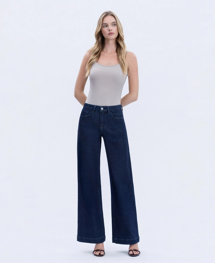 Woman wearing a white tank top and dark blue jeans on a white background