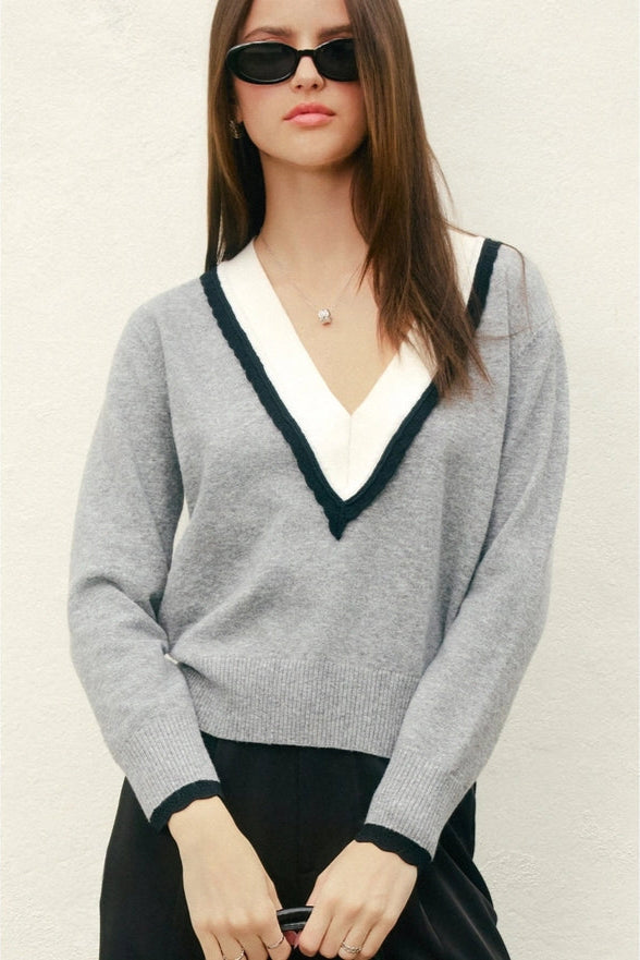 Woman wearing a gray sweater with a white collar against a plain background