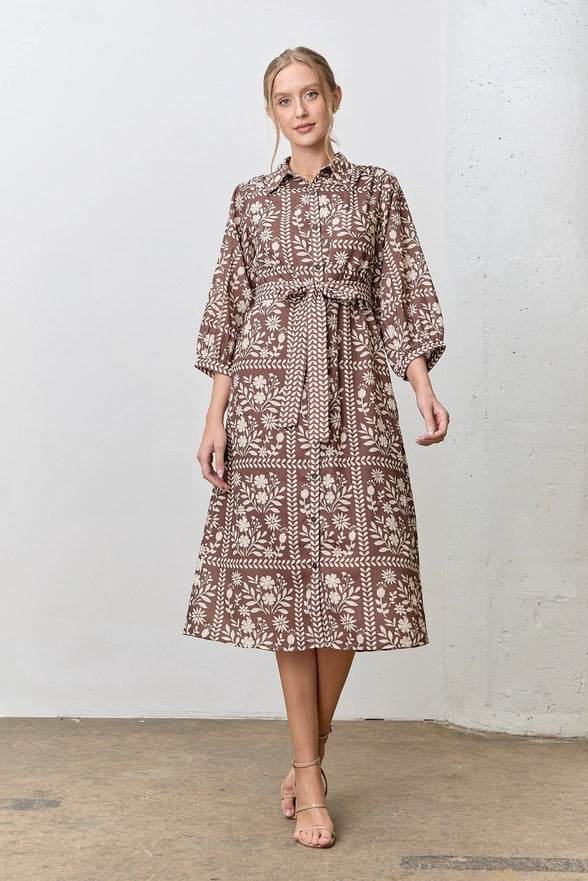 Woman wearing a patterned dress standing against a white wall.
