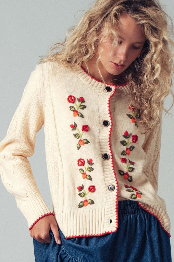 Woman wearing a cream cardigan with floral embroidery on a gray background