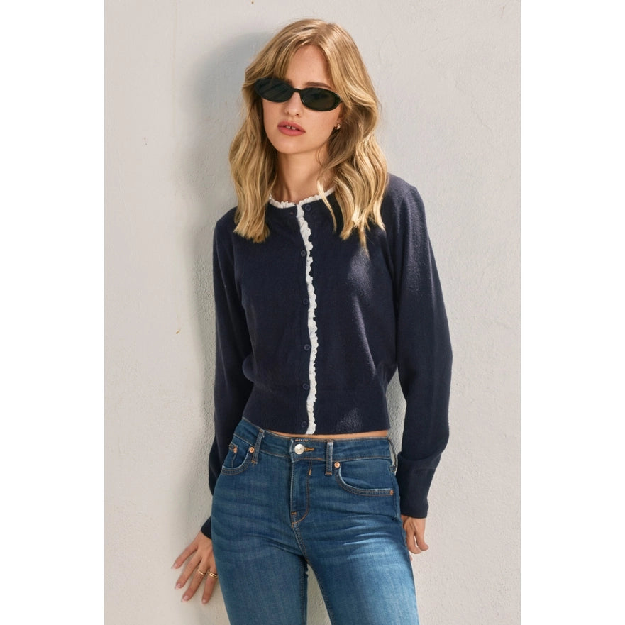 Woman wearing a navy sweater with white trim and blue jeans against a light gray background