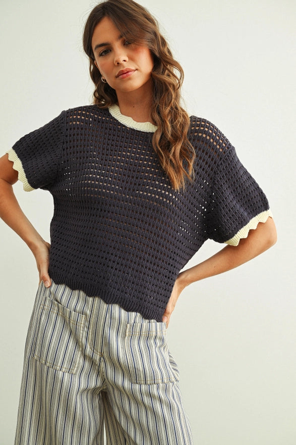 Woman wearing a dark blue crochet top with white trim on a plain background