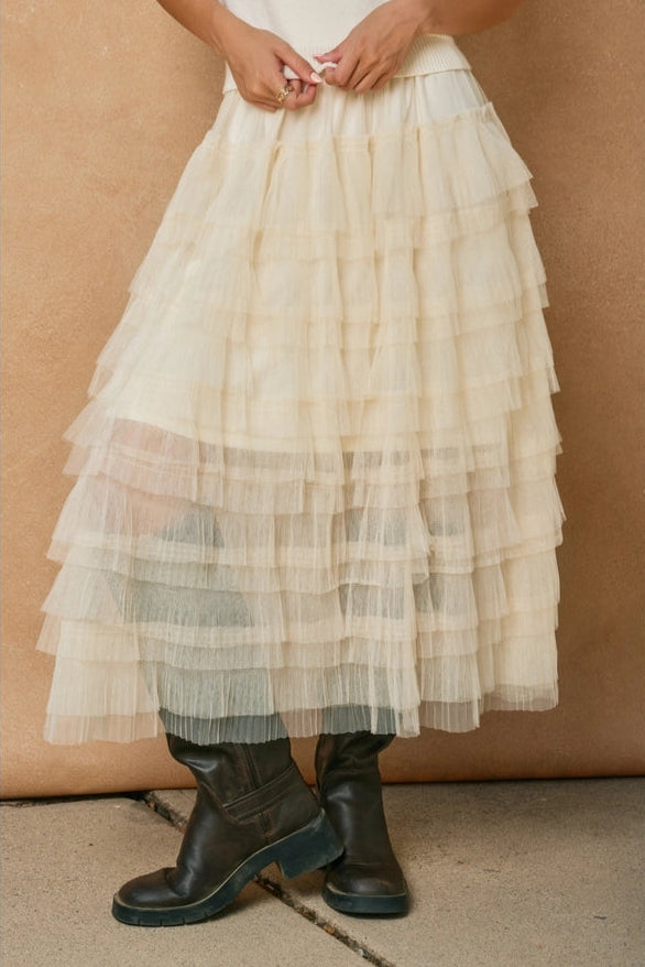 Person wearing a layered beige skirt with black boots against a beige background