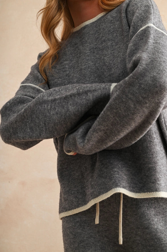 Gray sweatshirt with white trim worn by a person on a beige background