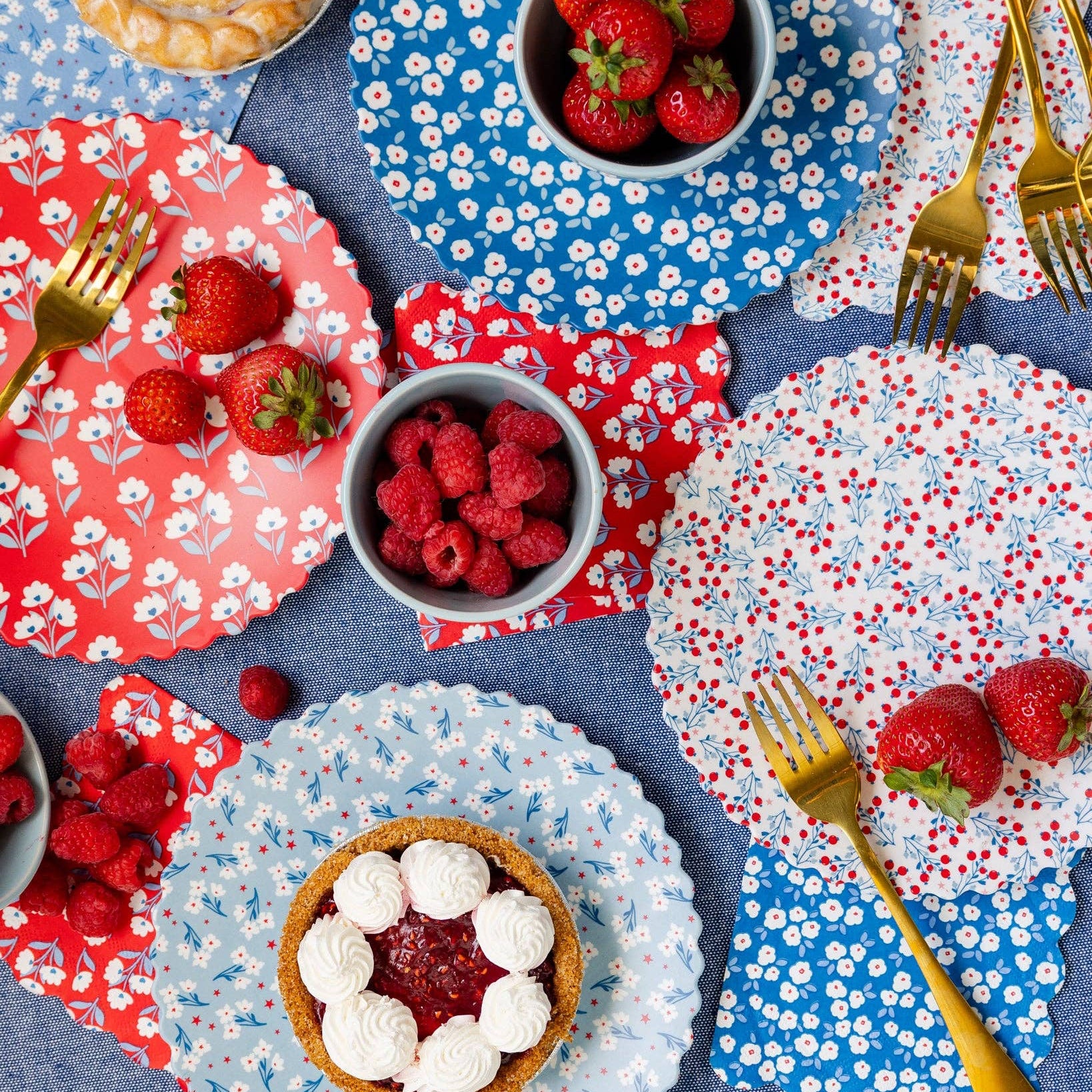 Dessert table with floral-patterned plates, bowls of berries, and pastries on a blue tablecloth.