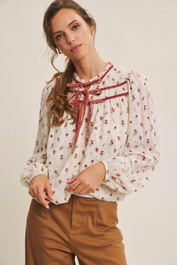 Woman wearing a floral blouse with a red ribbon and brown pants on a beige background