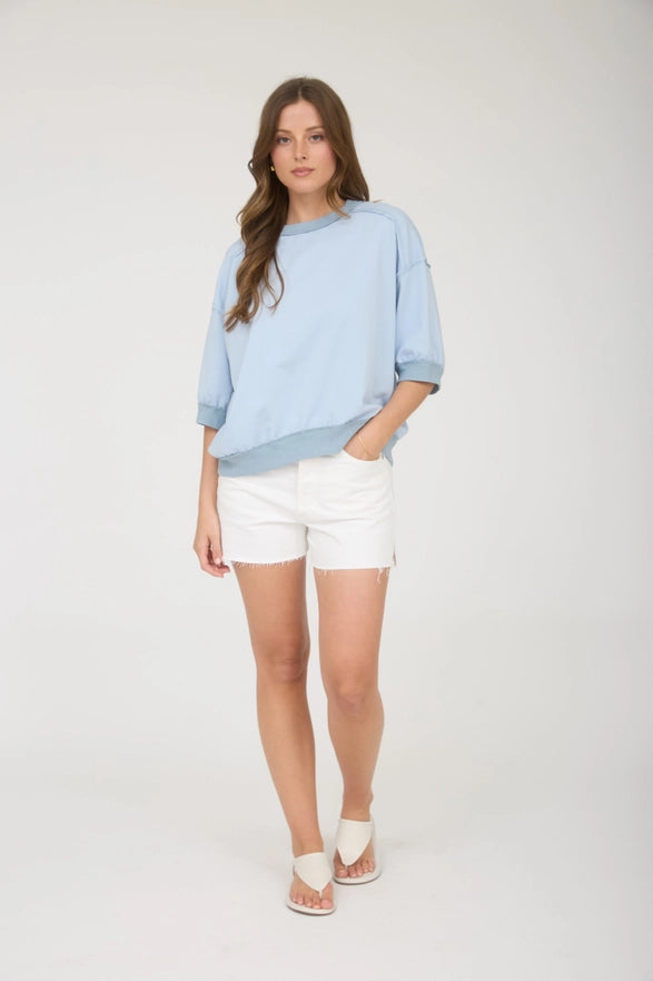 Woman wearing a light blue sweater and white shorts on a white background