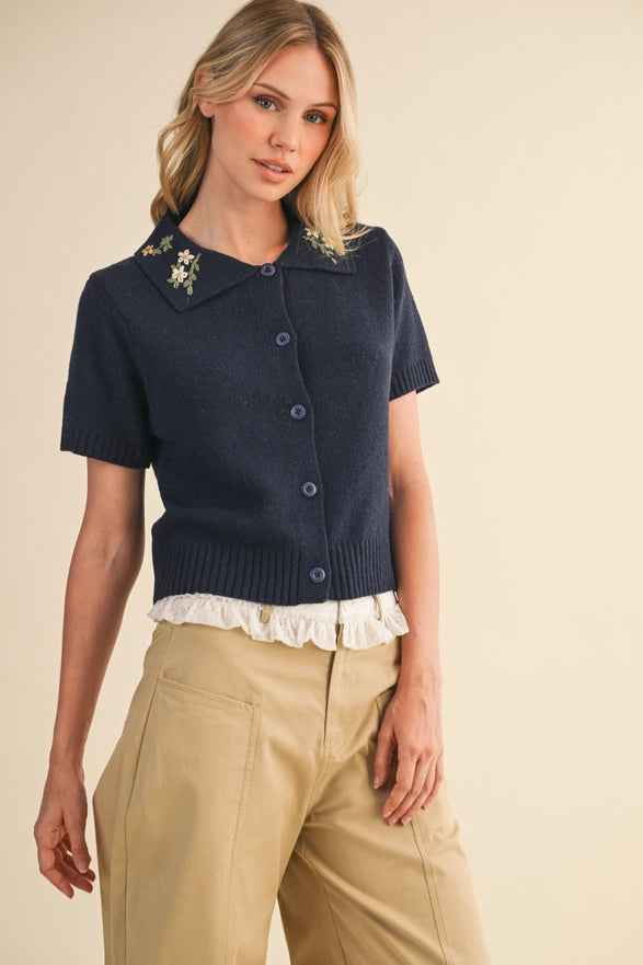 Woman wearing a navy blue short-sleeve cardigan with floral details on a beige background