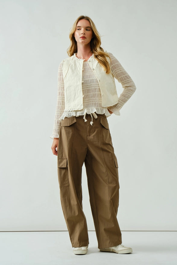Woman wearing a white top, beige vest, and brown cargo pants on a white background