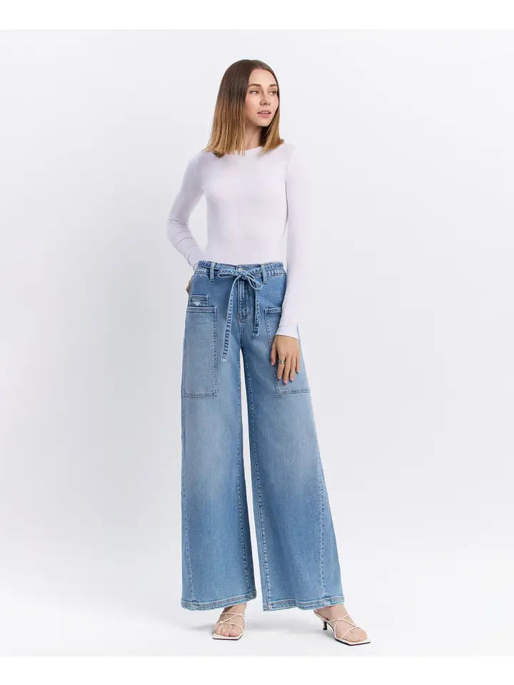Woman wearing light blue wide-leg jeans and a white top on a white background