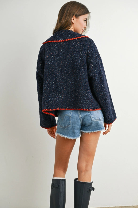 Person wearing a dark blue jacket with red trim, denim shorts, and black rain boots on a plain background